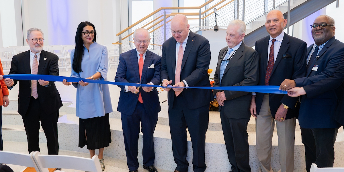A group of formally dressed individuals participates in a ribbon-cutting ceremony inside a modern, well-lit building.